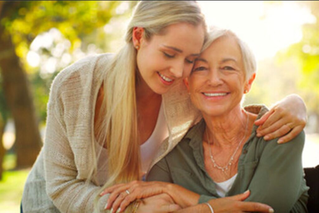 A white mother and daughter smile and embrace facing the camera.