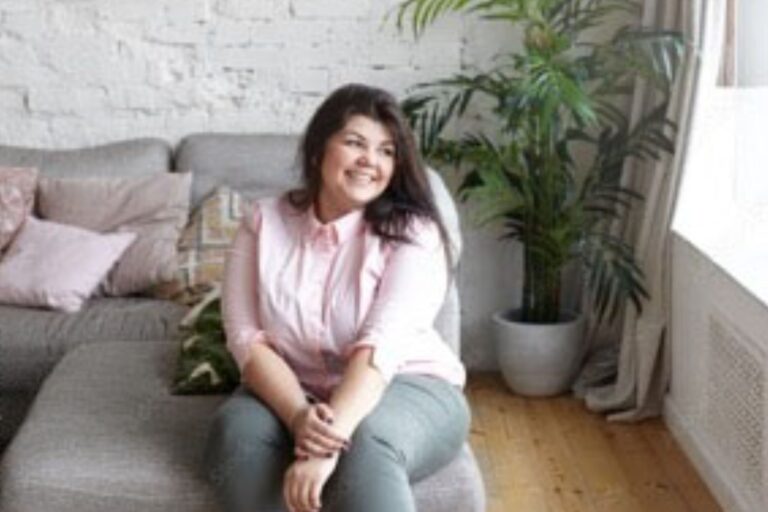 A white woman in her twenties smiles and looks across the room