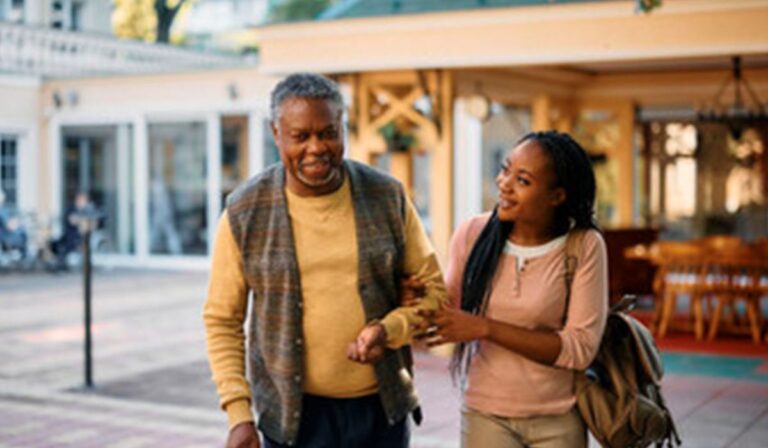 A smiling Black father in his fifties is escorted across the street by his smiling Black daughter.