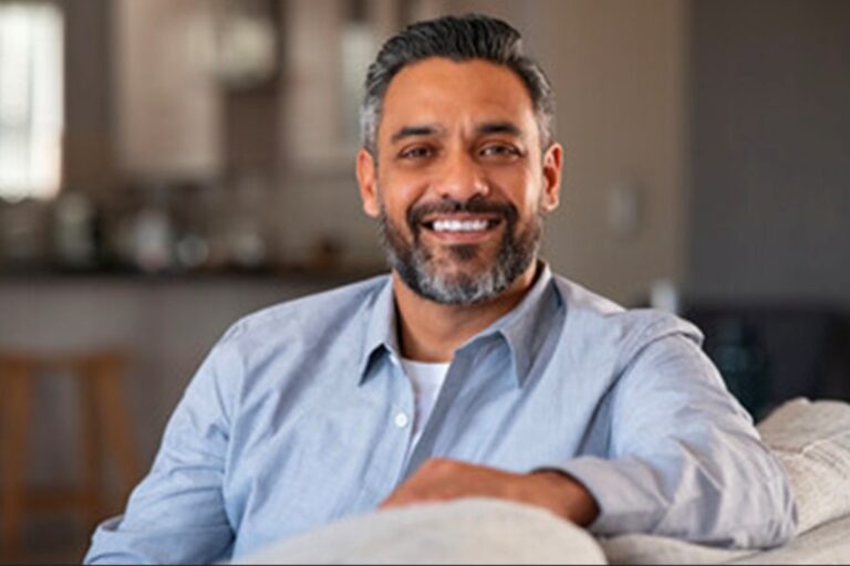 An Hispanic man with a beard in business causal clothing smiles into the camera.